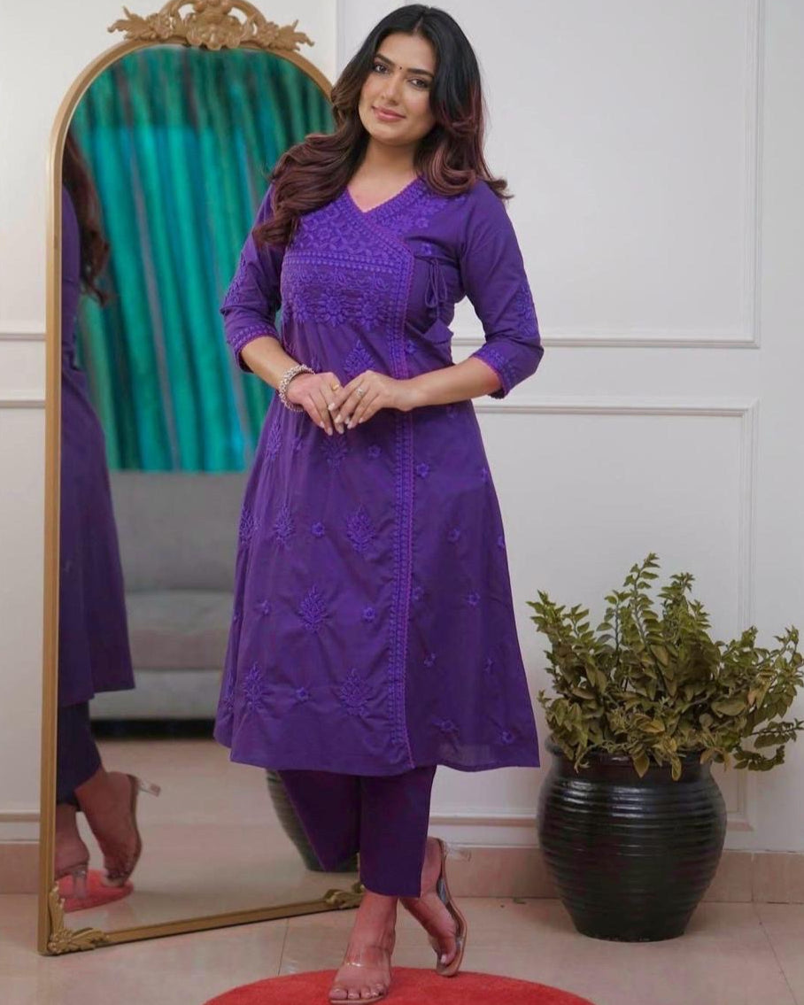 Woman in a purple outfit standing in front of a mirror in a room with a plant.